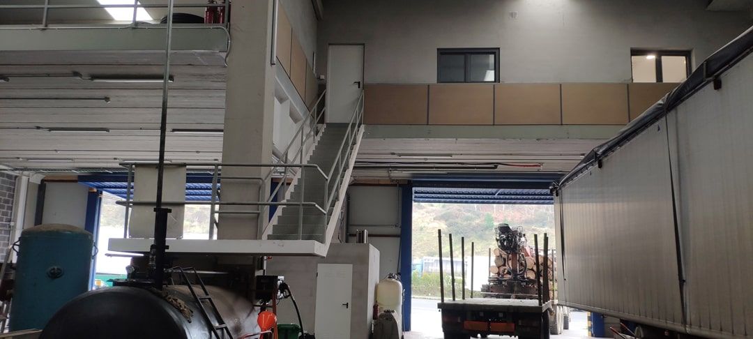 Interior de almacén industrial con escaleras, pasarela elevada y abertura para muelle de carga de camiones.
