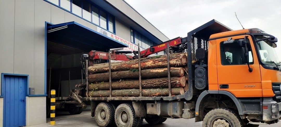 Camión maderero naranja cargado con madera cortada en la zona de carga de un almacén.