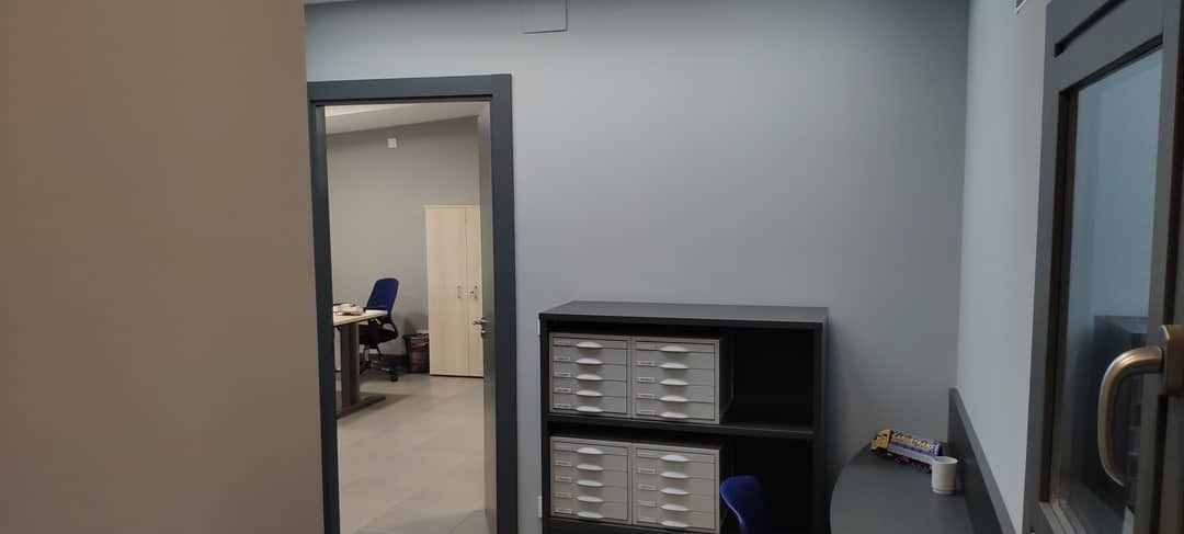 Pasillo de oficina con pared gris, puerta abierta y estante para guardar archivos y suministros.