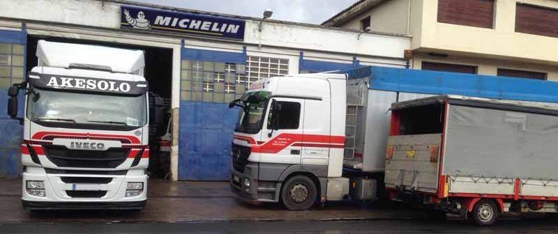 Tres camiones de reparto estacionados frente a un taller de servicio Michelin en una calle mojada.