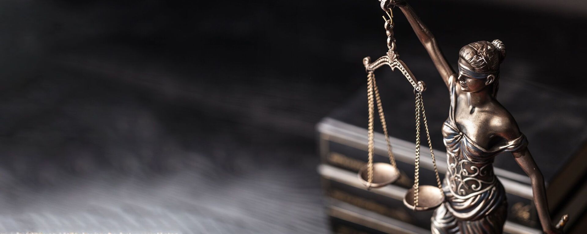 Statue der Justitia mit Waage vor dunklem Hintergrund.