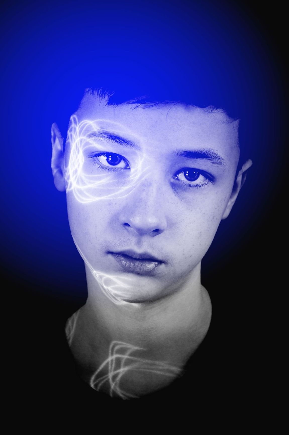 Una persona joven con energía azul y blanca brillante alrededor de su cabeza y rostro contra un fondo negro.