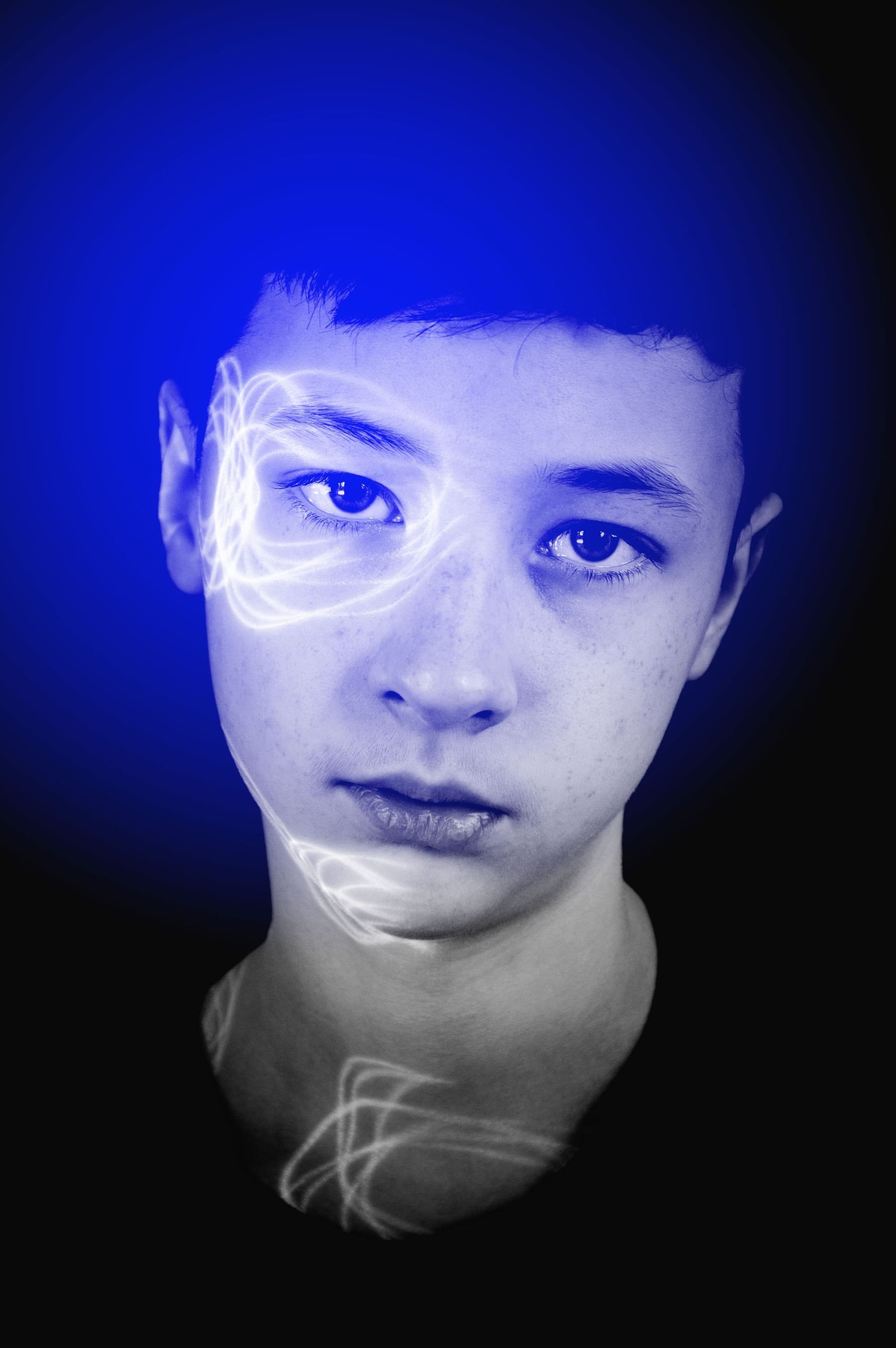 Una persona joven con energía azul y blanca brillante alrededor de su cabeza y rostro contra un fondo negro.