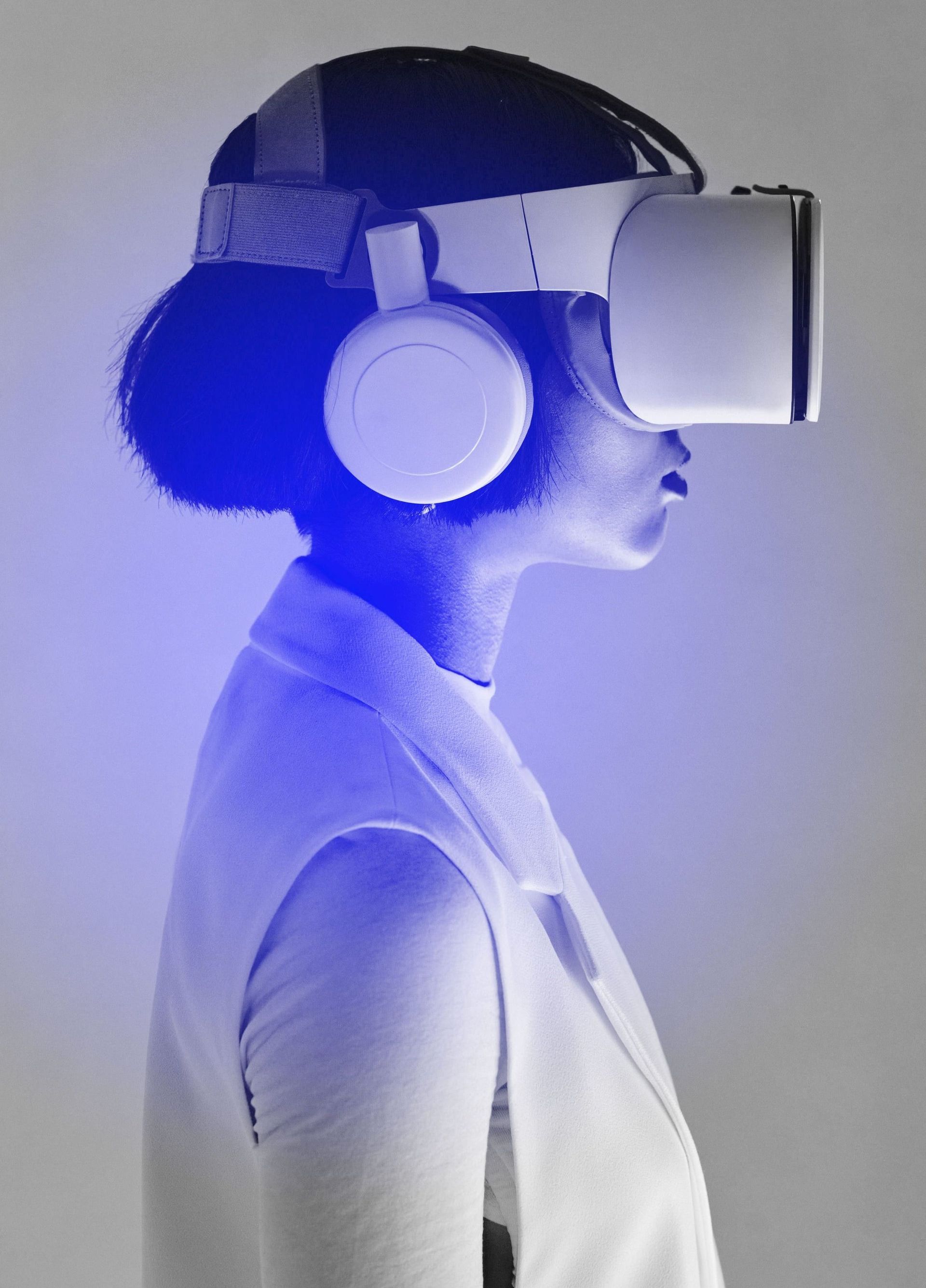 Mujer que usa un casco de realidad virtual y auriculares, bañada por luz azul, vista de perfil.