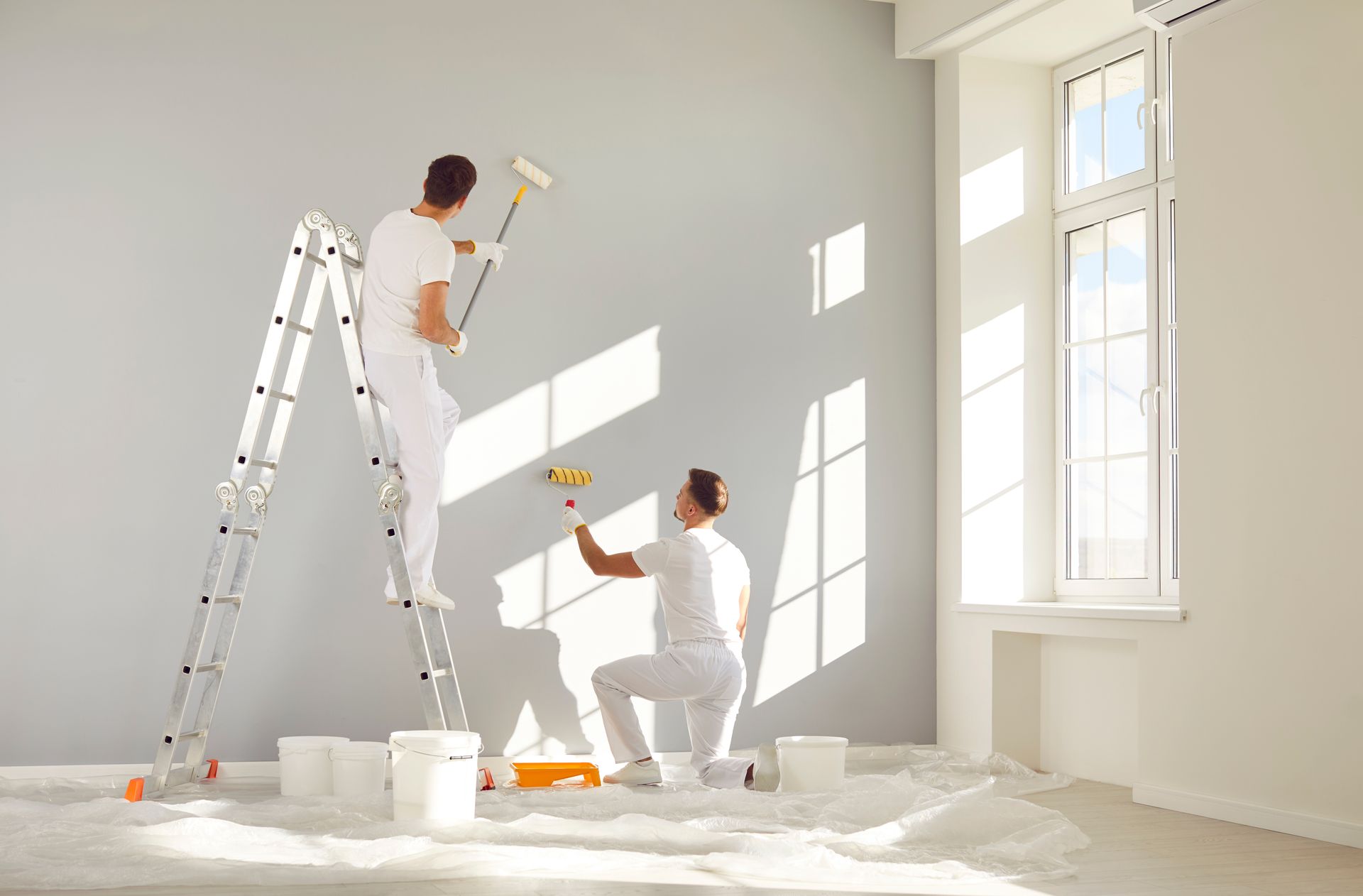 Deux hommes en train d'appliquer une peinture grise sur un mur