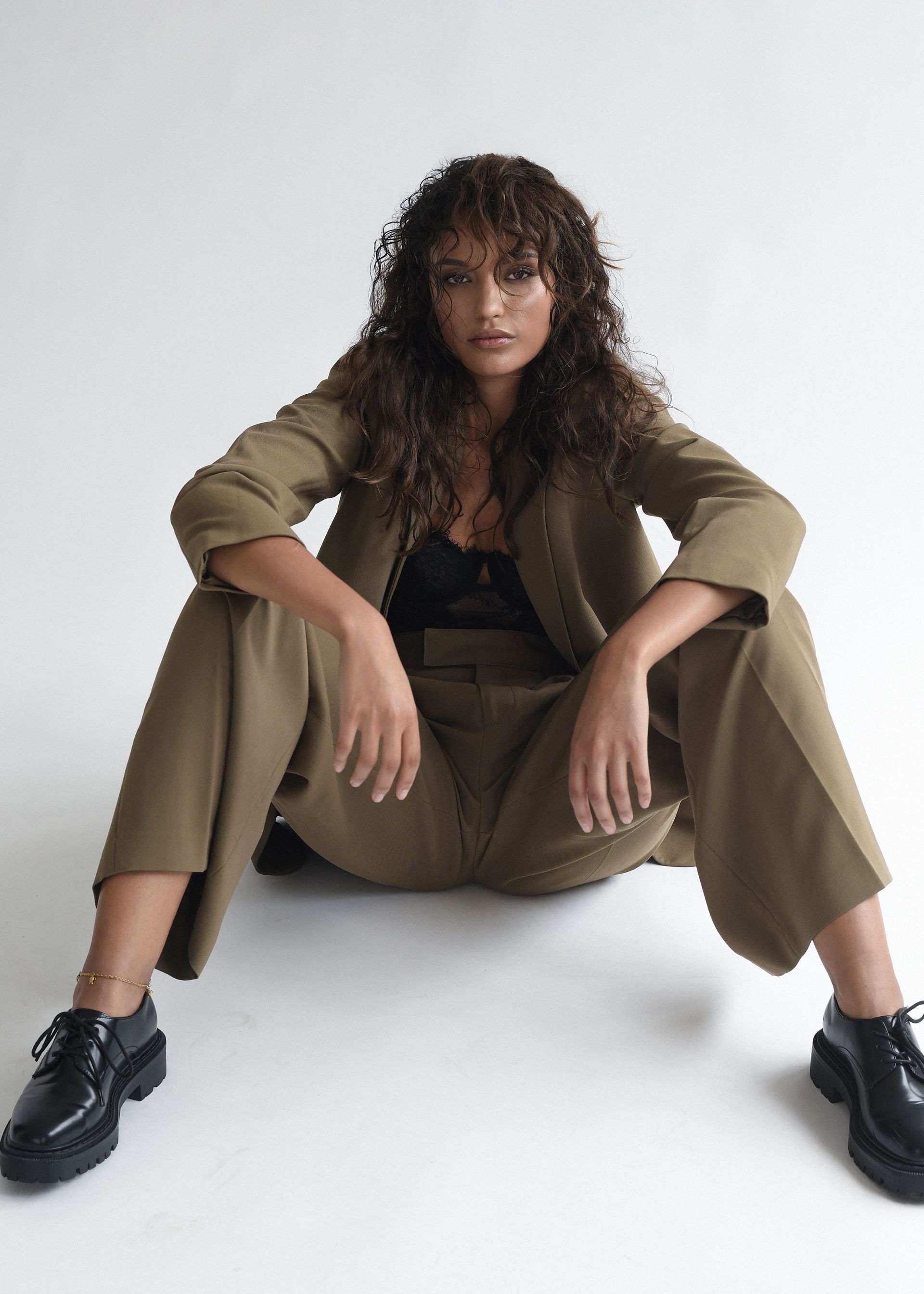 Eine Frau im Anzug sitzt mit überkreuzten Beinen auf dem Boden.