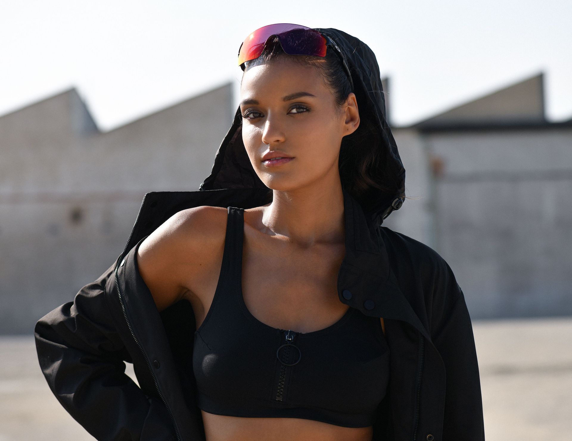 Eine Frau mit Sonnenbrille und schwarzer Jacke steht vor einem Gebäude.