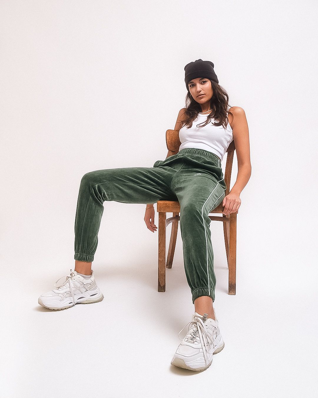 Eine Frau in einem weißen Tanktop und grünen Hosen sitzt auf einem Stuhl.