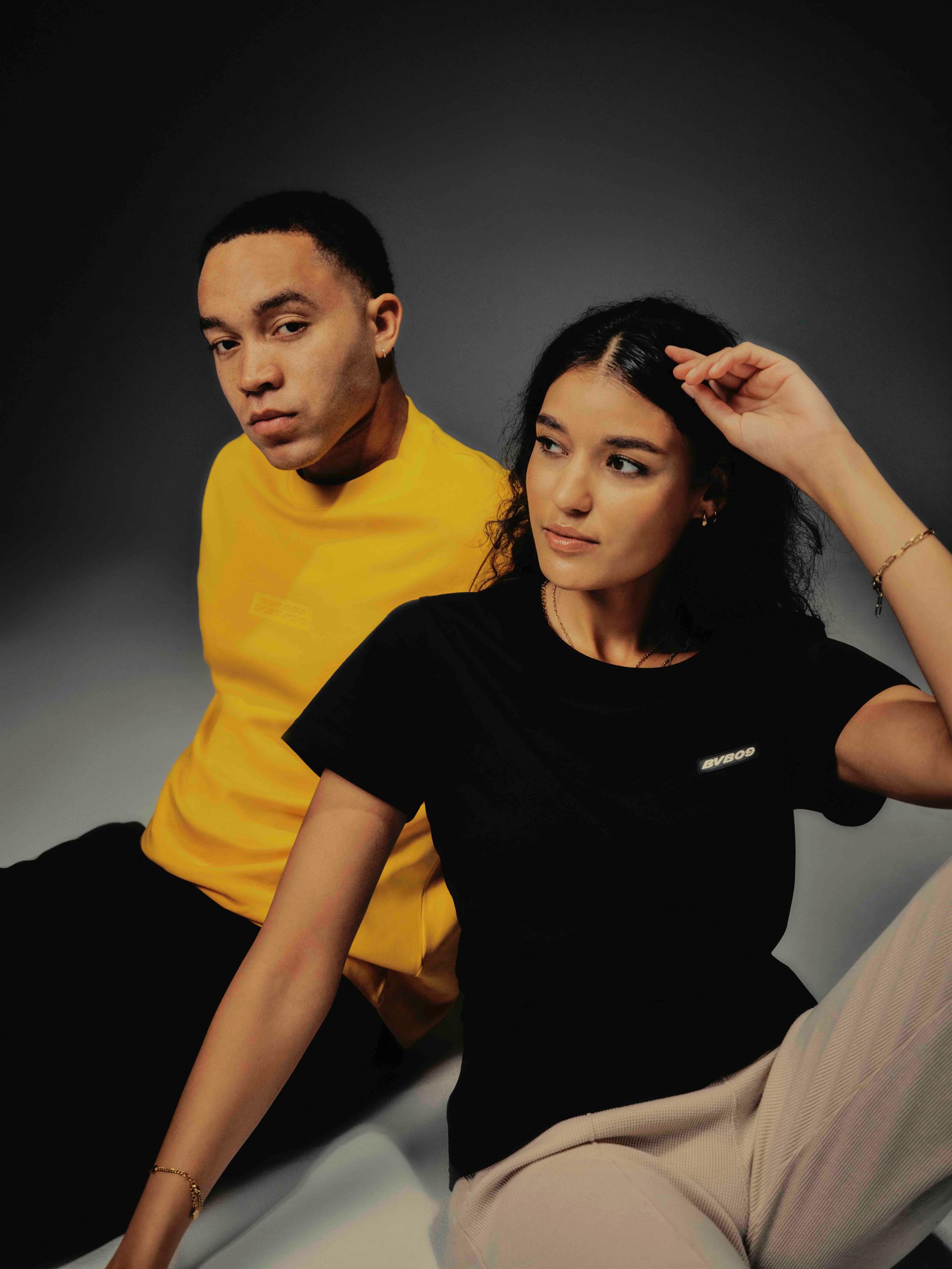 Mann im gelben Hemd und Frau im schwarzen Hemd sitzen und schauen weg.