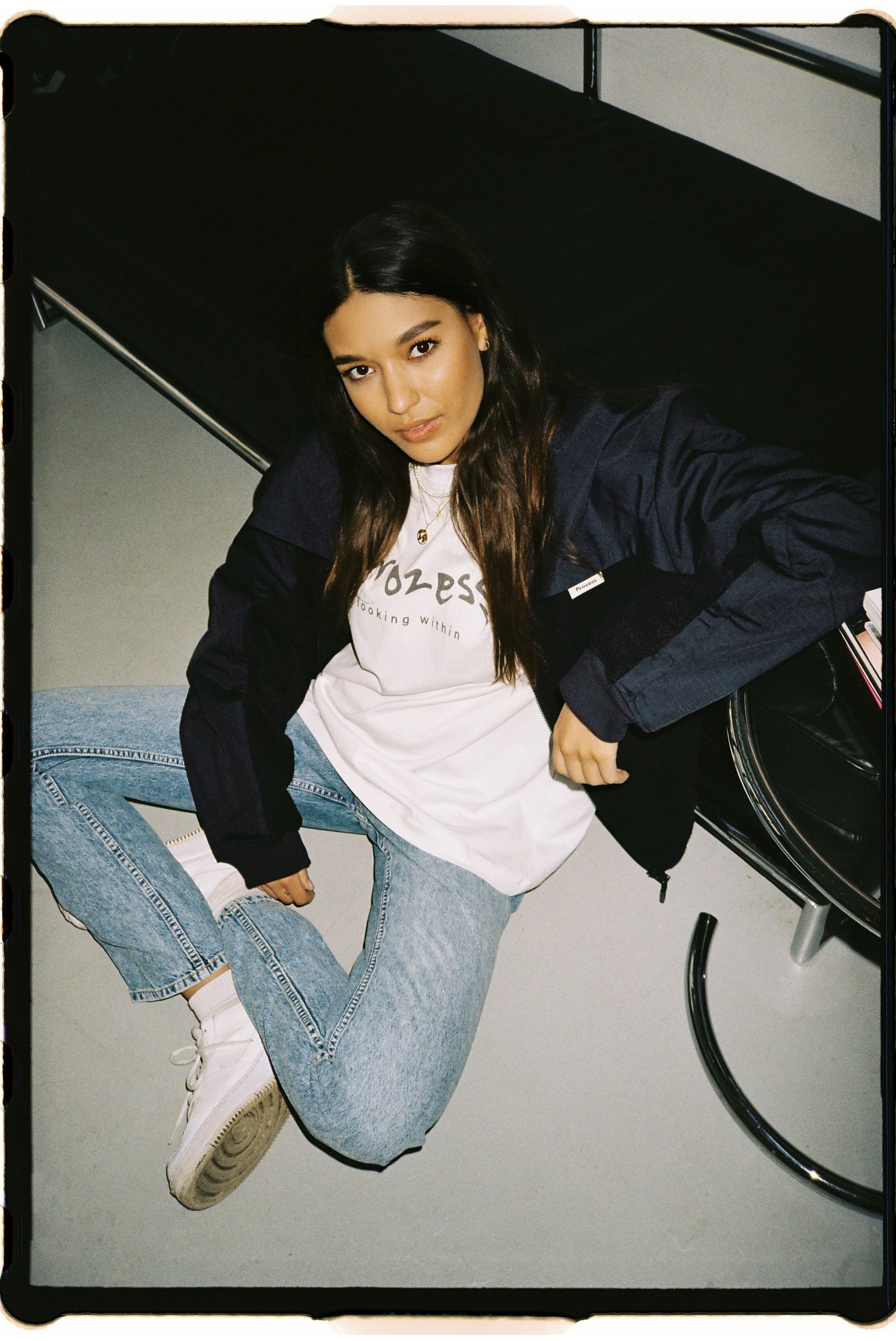 Eine Frau in Jeans und weißem Hemd sitzt auf dem Boden.