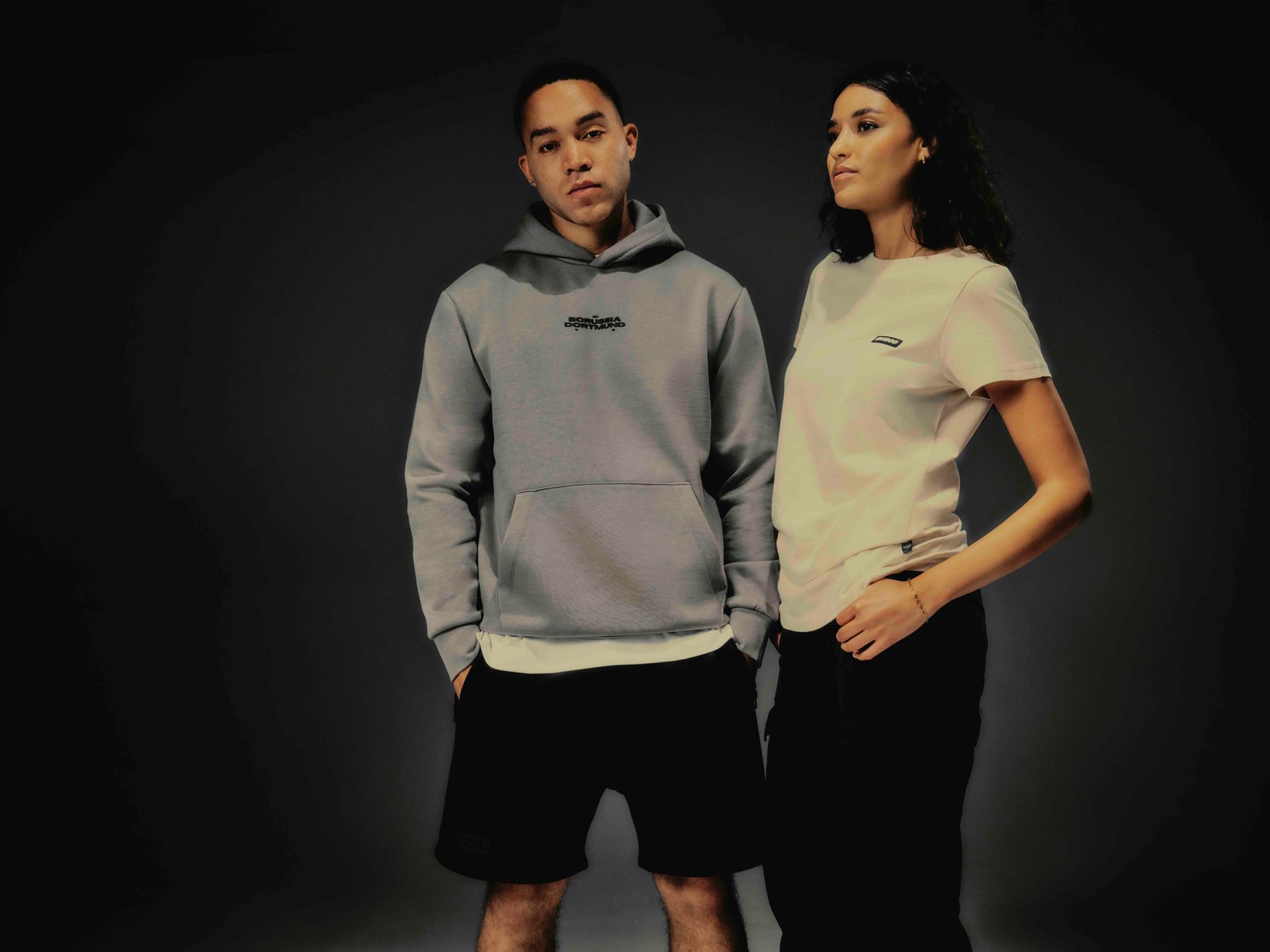 Mann und Frau in Freizeitkleidung stehen vor grauem Hintergrund.