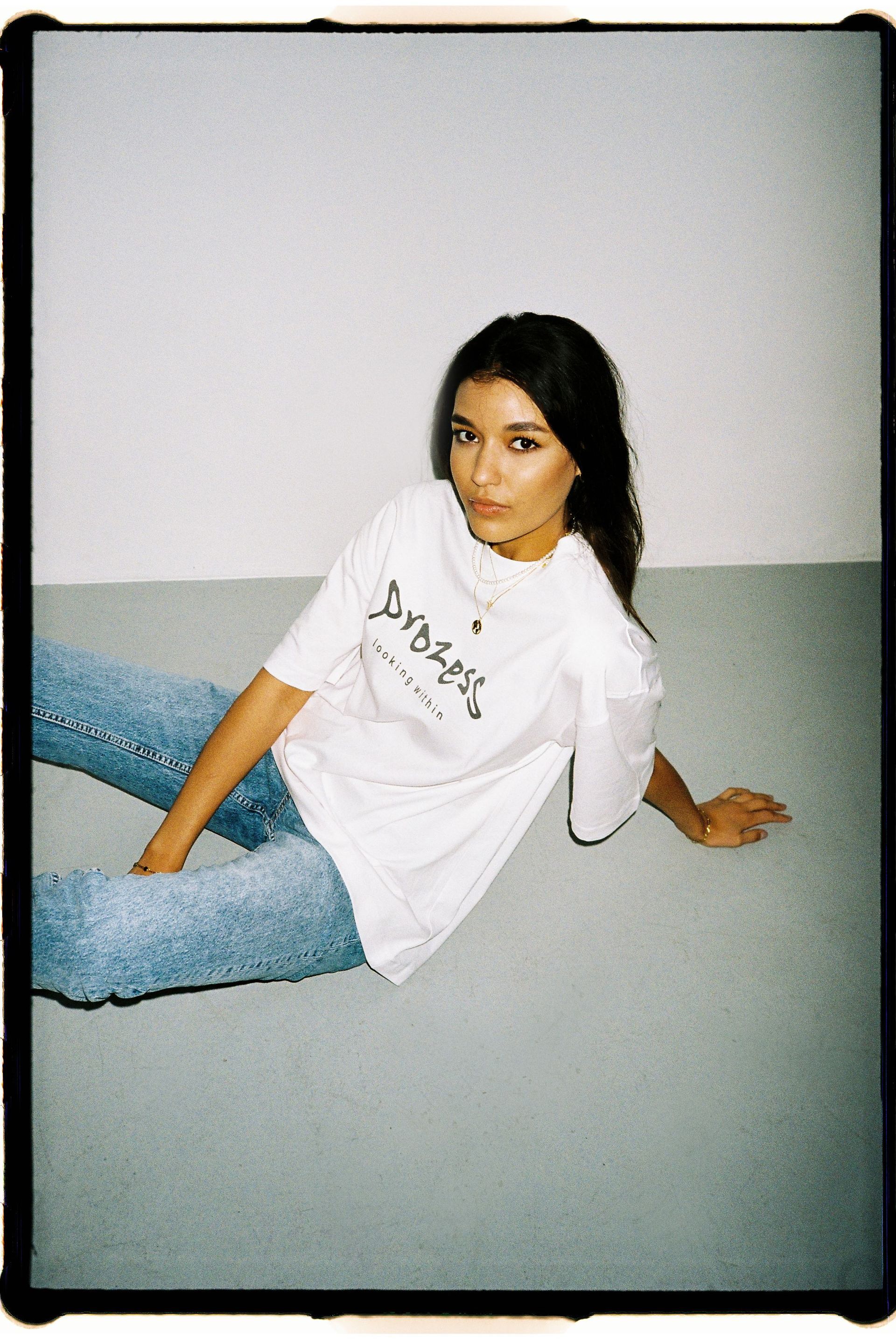 Eine Frau sitzt in einem weißen T-Shirt und Jeans auf dem Boden.