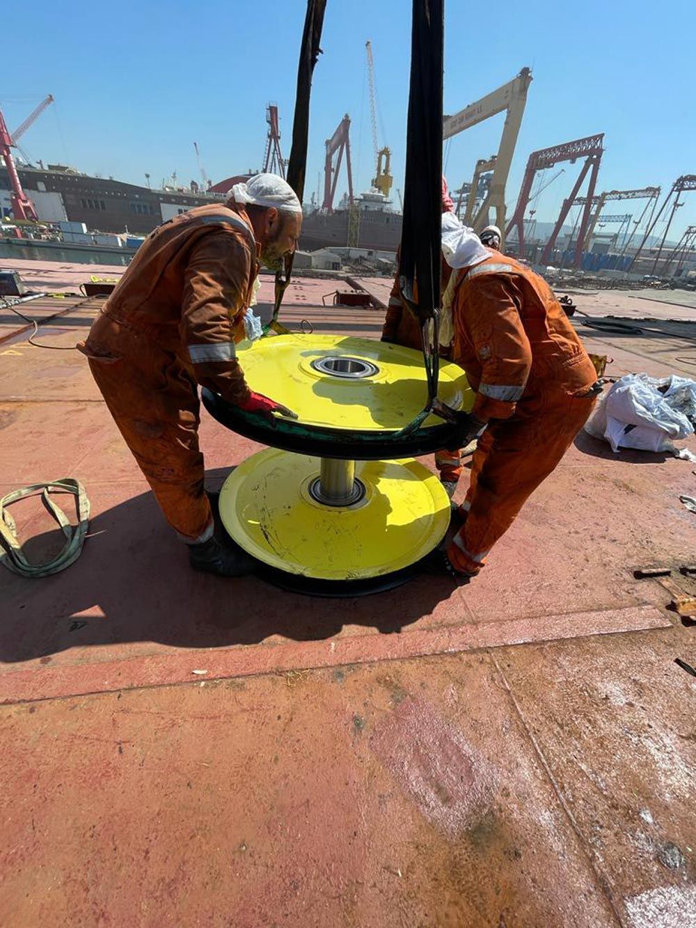 Zwei Männer in orangefarbenen Overalls arbeiten an einem großen gelben Objekt.