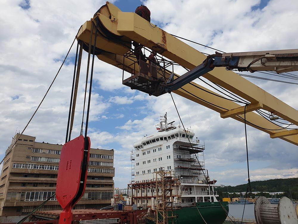 Ein großer Kran hebt ein großes Schiff ins Wasser.