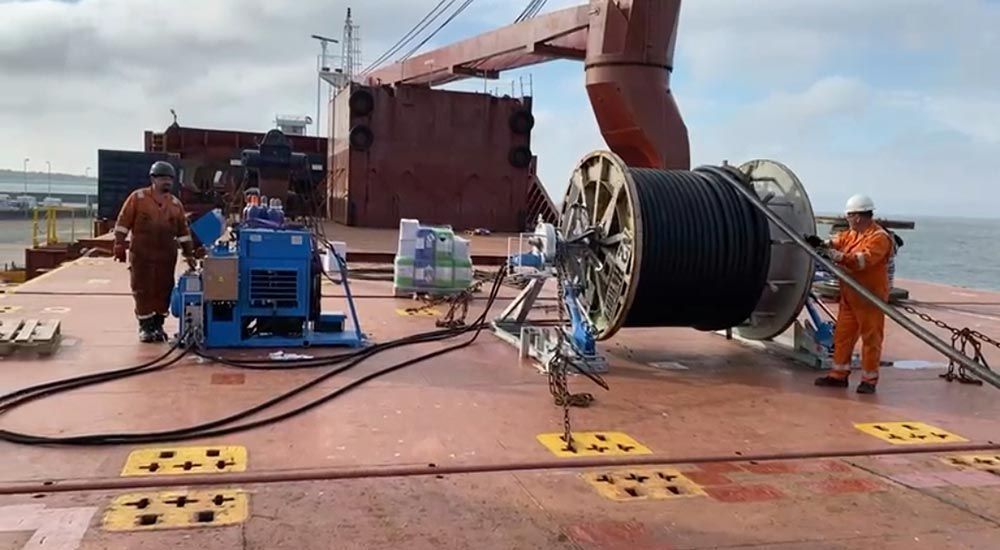 Eine große Kabelspule wird auf ein großes Schiff geladen.