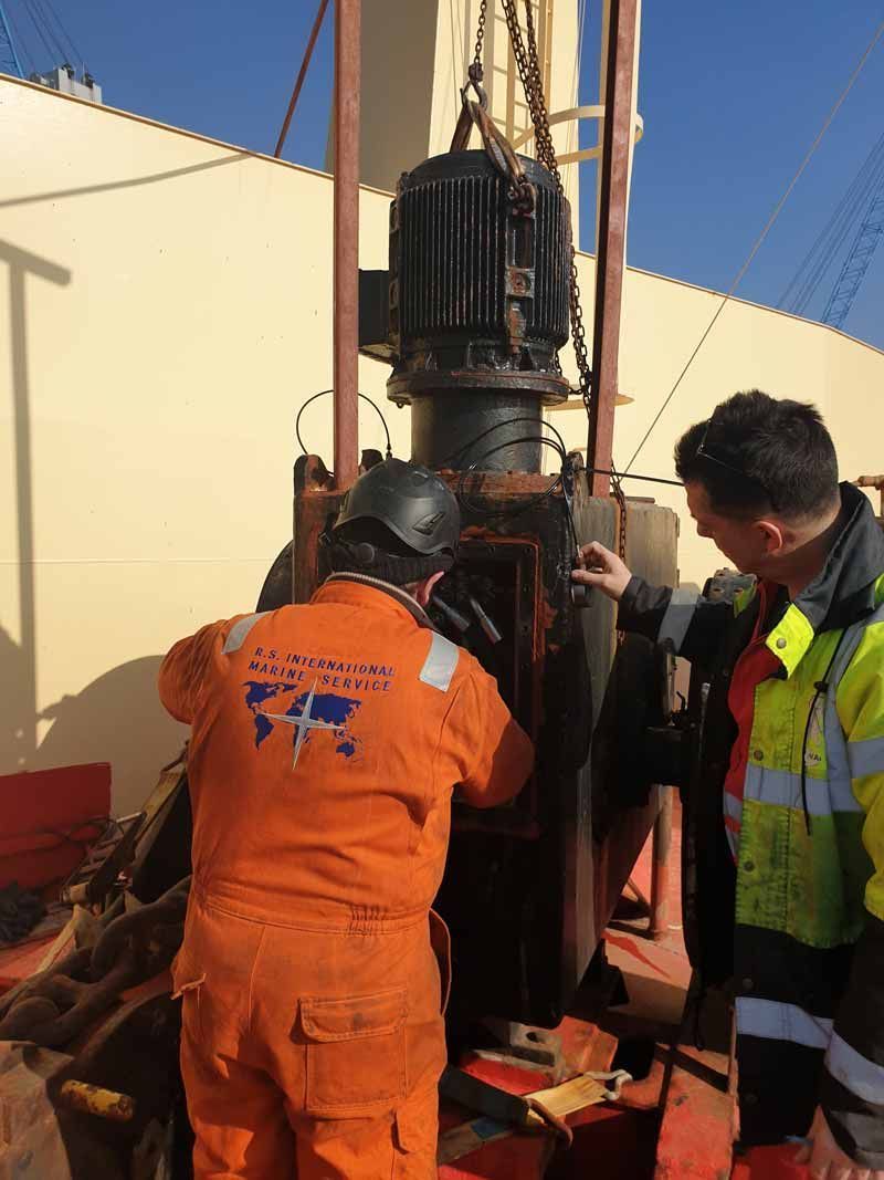 Zwei Männer in orangefarbenen Overalls arbeiten an einer Maschine.