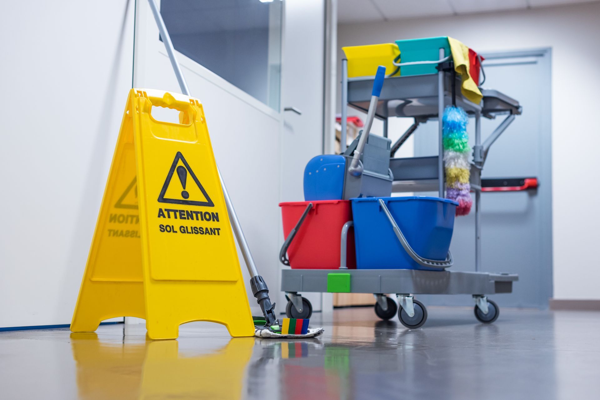 Panneau jaune sol mouillé à côté d'un chariot de nettoyage dans un couloir d'hôpital.