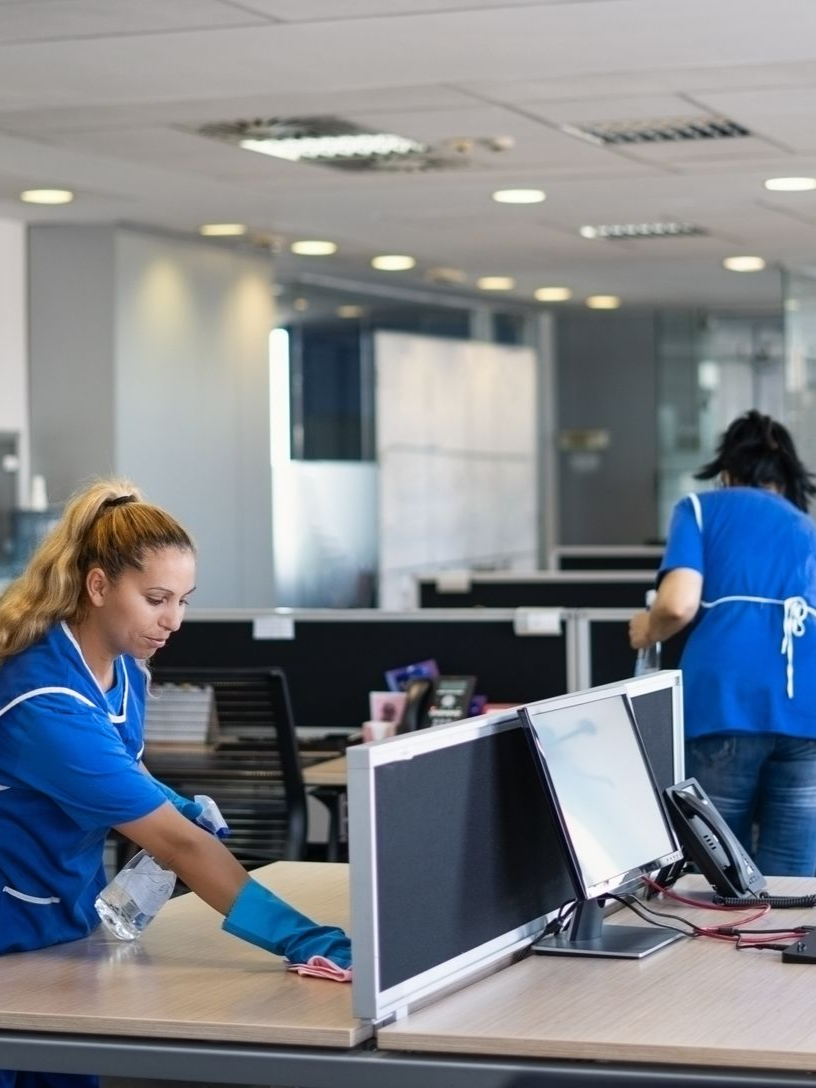 Deux personnes en uniforme bleu nettoient des bureaux dans un espace de travail moderne.