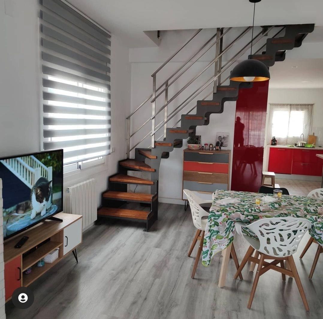 Una sala de estar con escaleras, una mesa, sillas y un televisor.