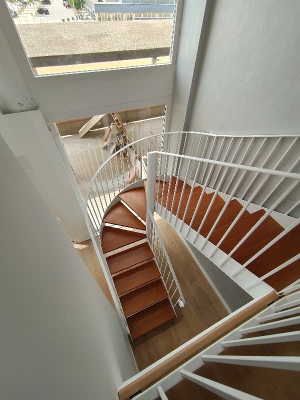 Una escalera de caracol con escalones de madera y barandilla blanca.