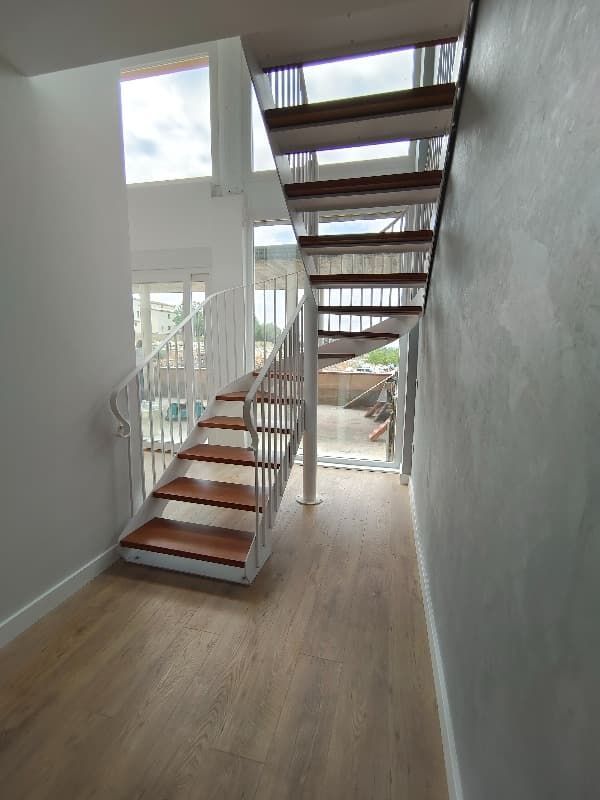 Una escalera de caracol en un pasillo con escalones de madera y barandilla blanca.