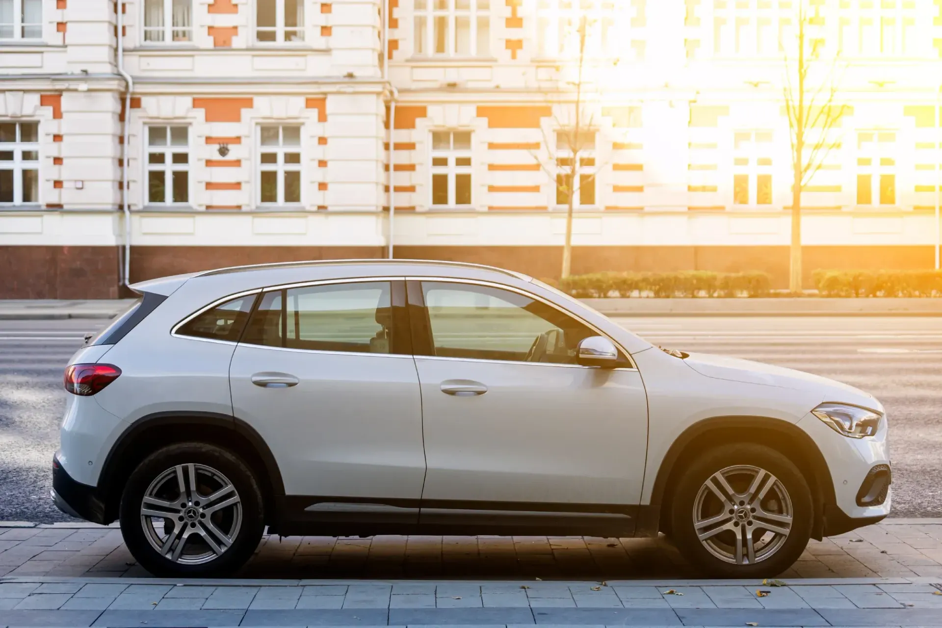 SUV blanco estacionado en una acera frente a un edificio en un día soleado.