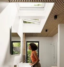 Una mujer está parada en un baño mirando hacia el tragaluz.