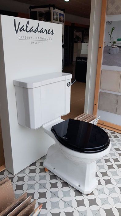 Un inodoro blanco con un asiento negro está sentado frente a una pared que dice valadares.