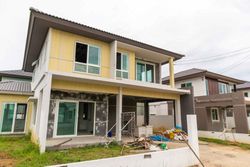 Casa de dos plantas en construcción con revestimiento amarillo, molduras grises y materiales de construcción en la fachada.