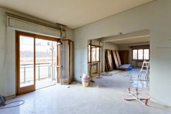 Habitación luminosa sin terminar con puertas corredizas de vidrio, estructura a la vista.
