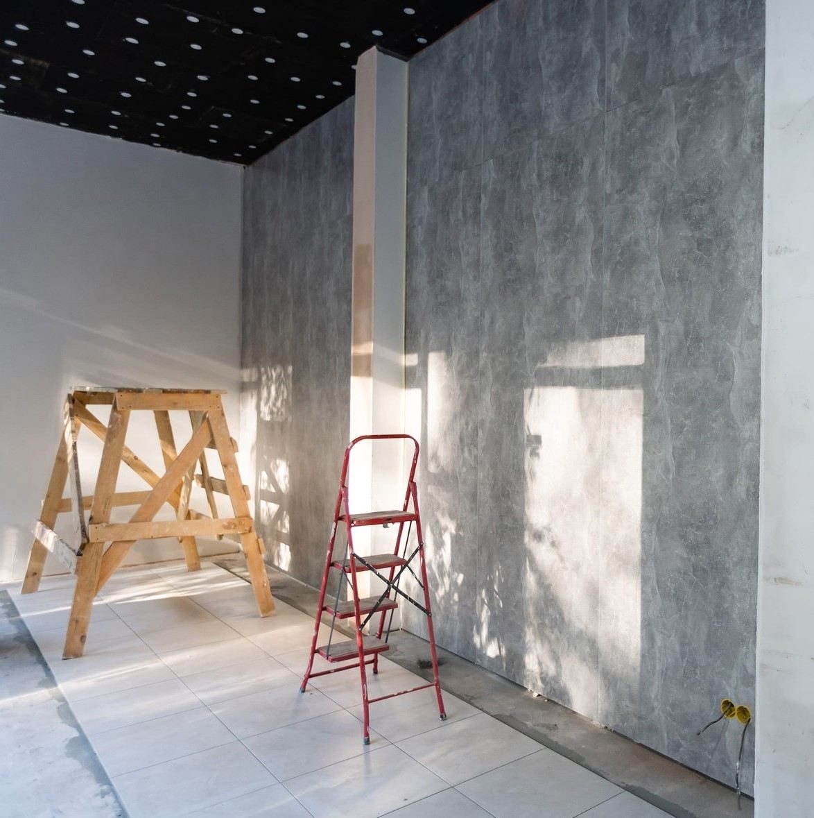 Habitación interior en obras, con dos escaleras contra paredes grises y un techo negro con luces que simulan estrellas.
