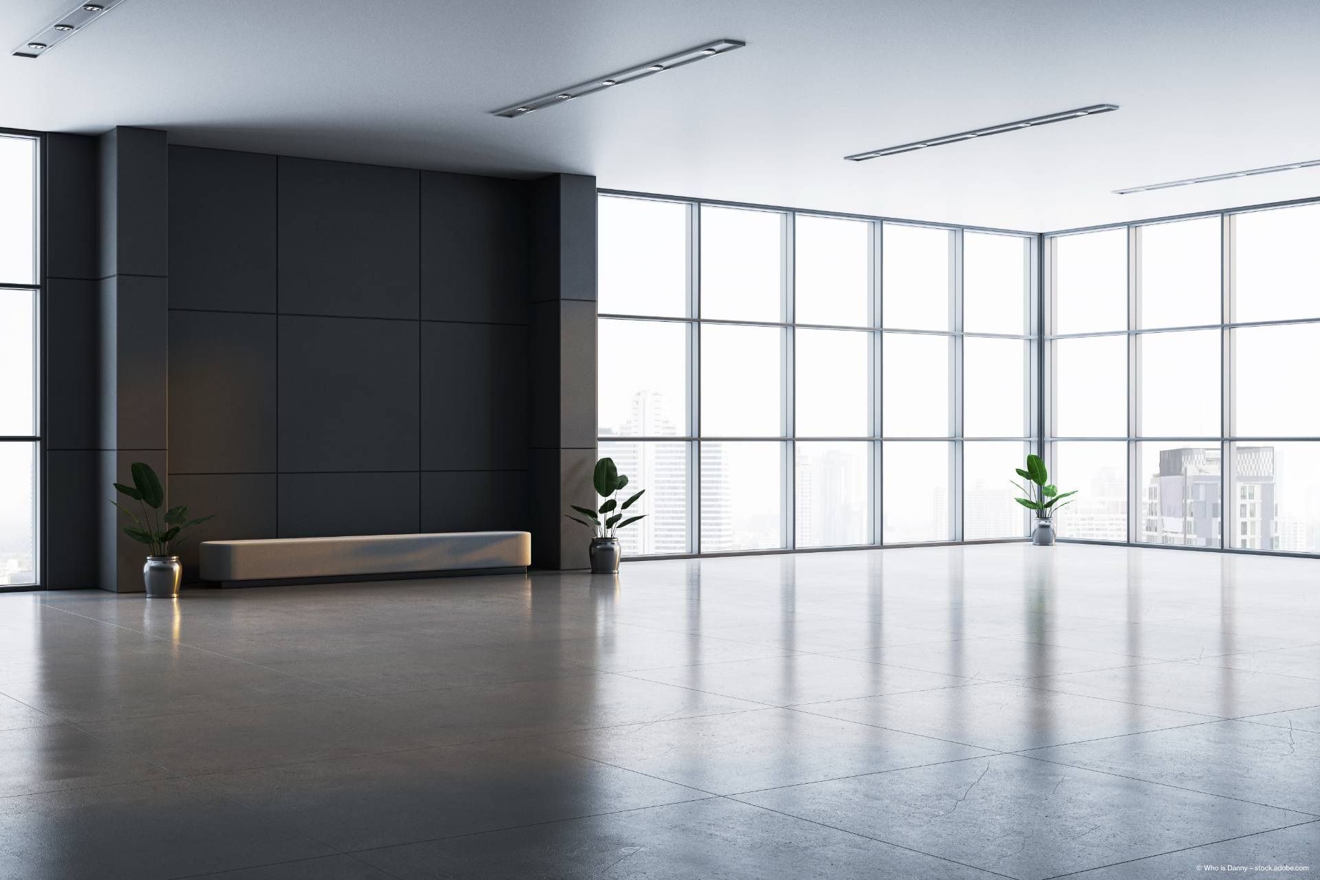 Minimalistisches Interieur eines modernen Büros mit großen Fenstern, einer schlichten grauen Sitzbank und Topfpflanzen sowie einem Betonboden.