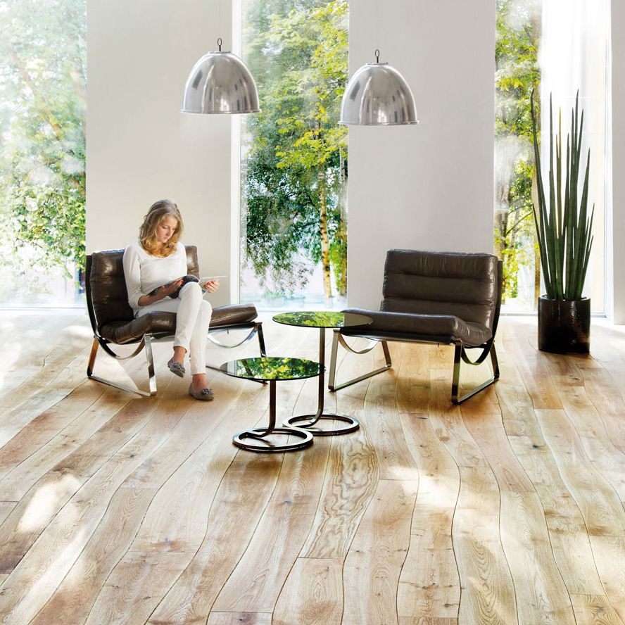 Eine Person im karierten Hemd schneidet einen Laminatboden entlang einer Wand zu und bereitet ihn für die Verlegung auf einem Holzboden vor.