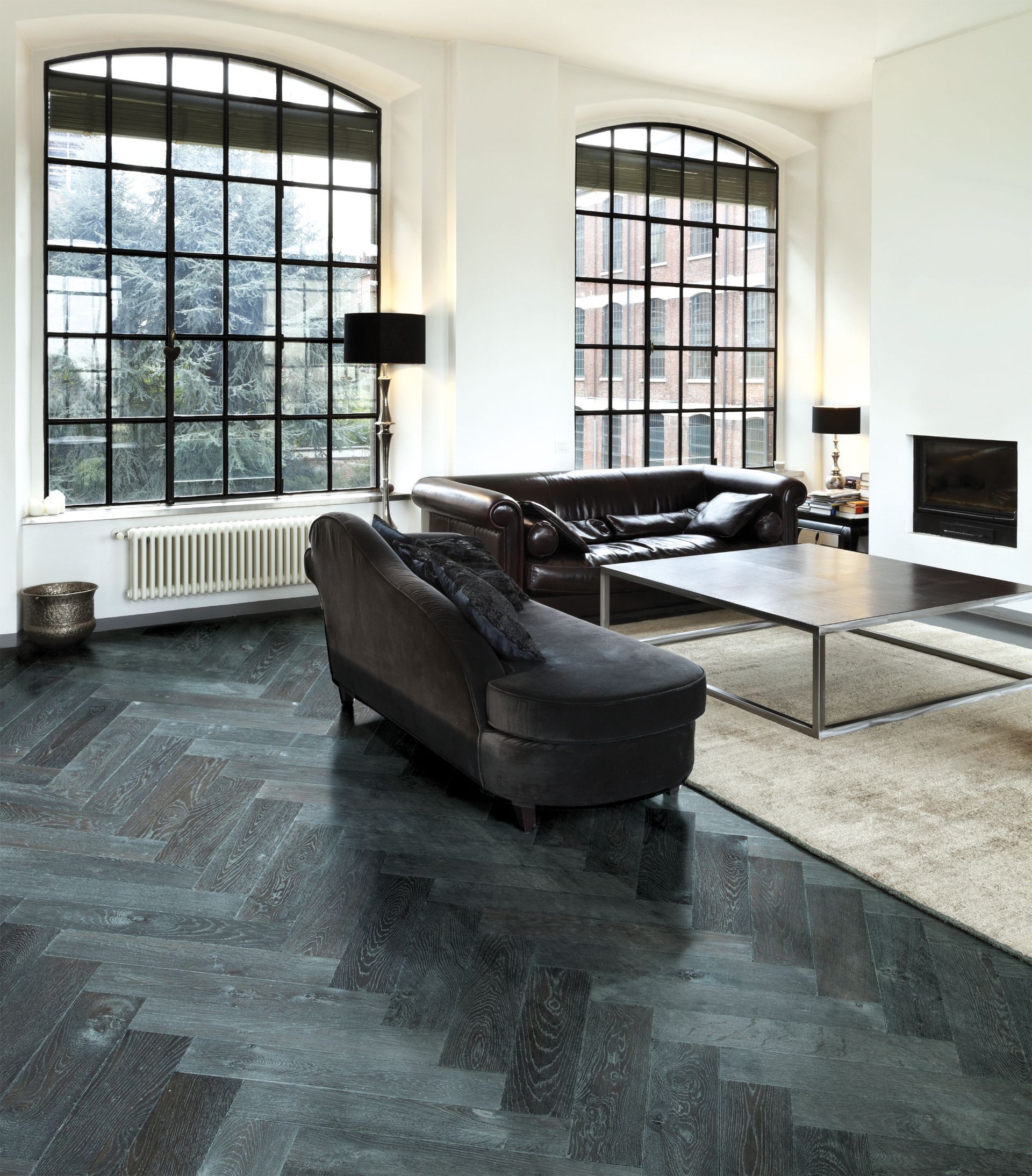 Ein dunkles Wohnzimmer: schwarzes Fischgrätenparkett, schwarze Sofagarnituren, große Fenster mit schwarzen Streben und weißen Wänden