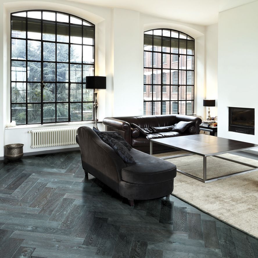 Ein dunkles Wohnzimmer: schwarzes Fischgrätenparkett, schwarze Sofagarnituren, große Fenster mit schwarzen Streben und weißen Wänden