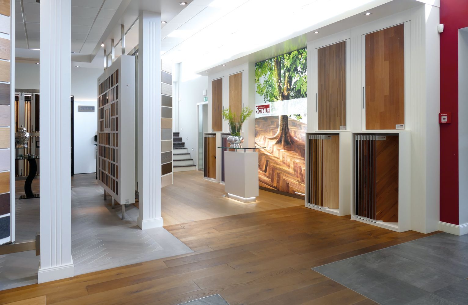 Ausstellungsraum mit verschiedenen Holzfußbodenmustern auf Regalen, mit einer eleganten Theke und einer Wand mit Designwörtern in deutscher Sprache.