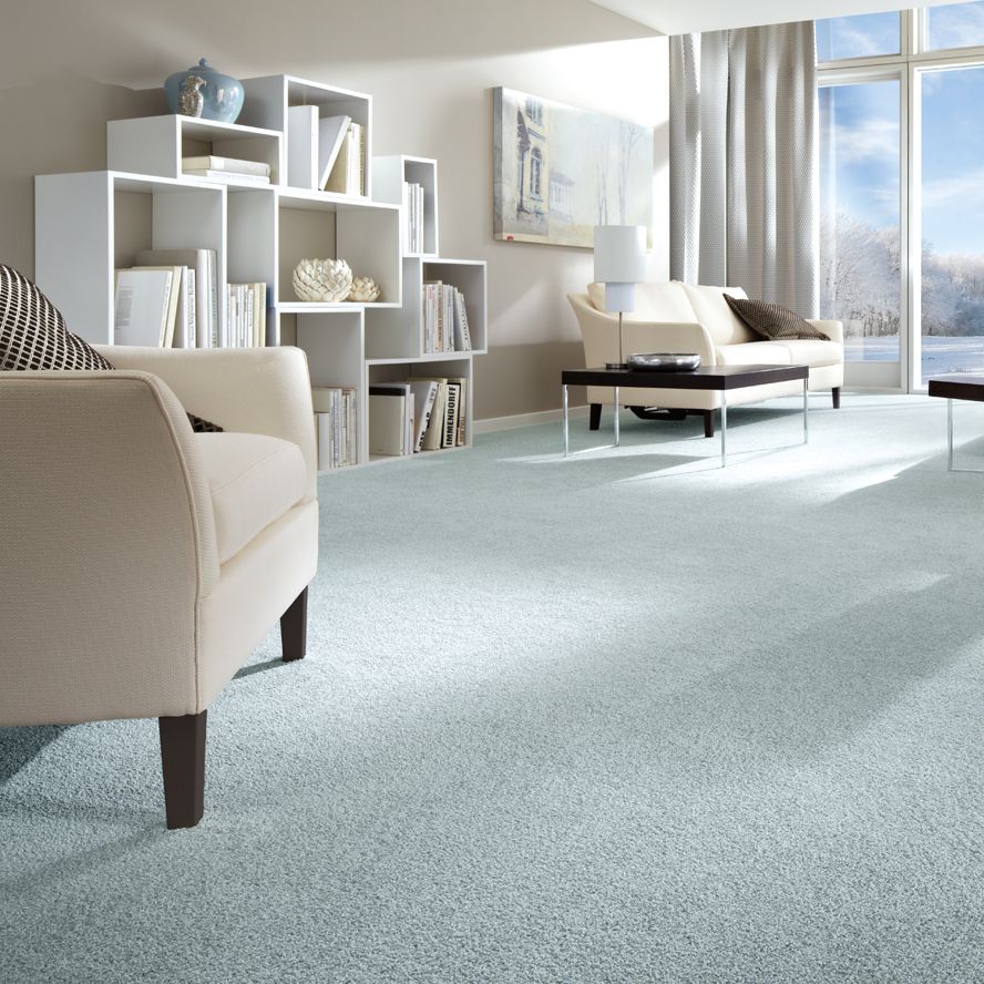 Ein Wohnzimmer im Beach-Look: beige Sitzmöbel, hellblauer Teppichboden und ein weißes Regal mit Büchern und Deko