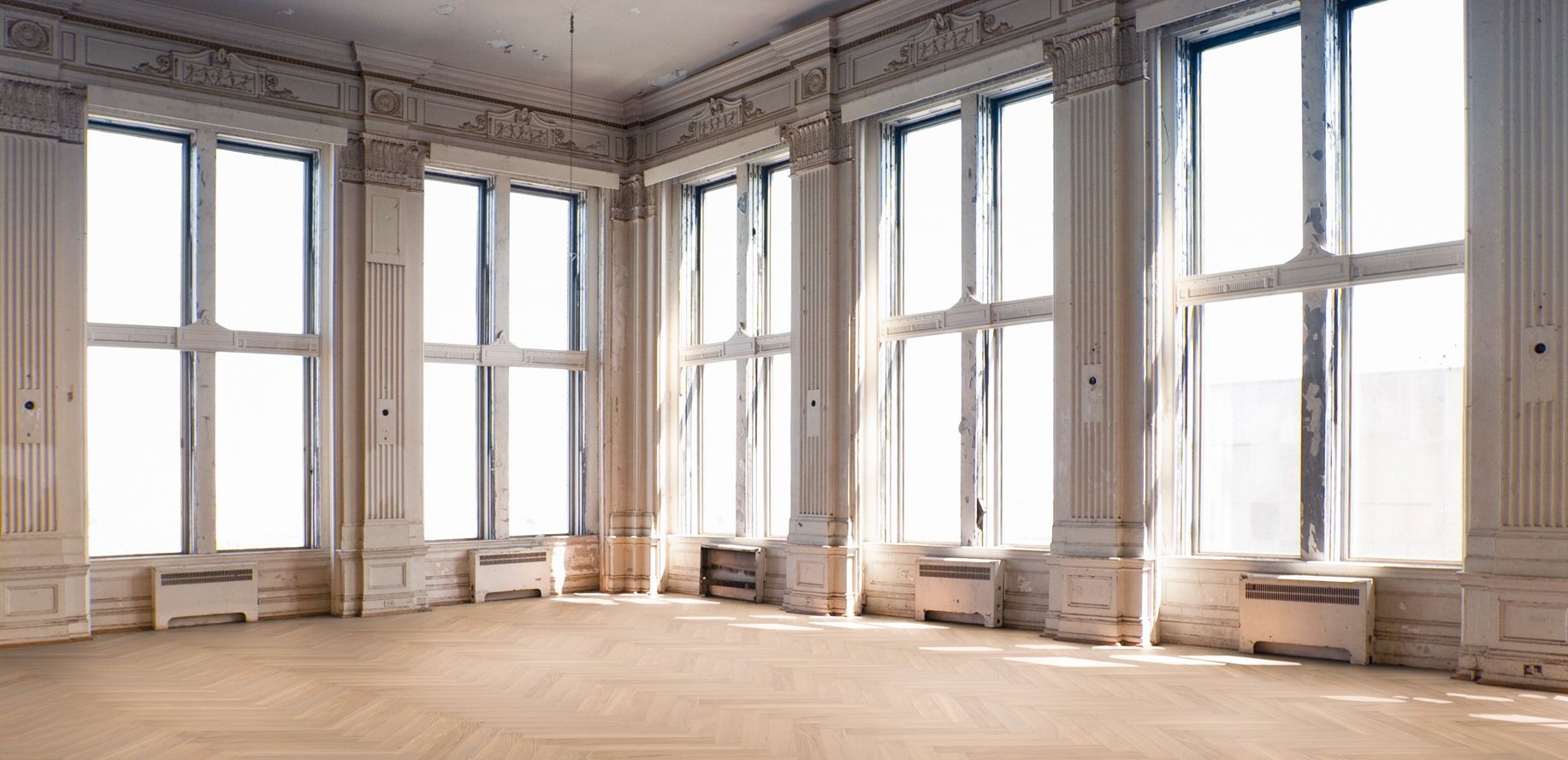 Ein historisch wirkender Raum mit sehr hohen Decken, Stuck und hellem Fischgrätenparkett