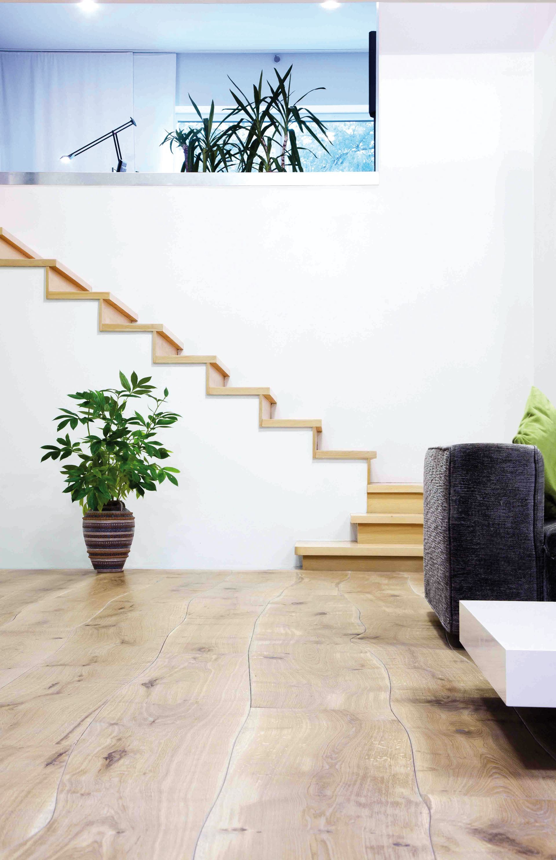 Helles, modernes Wohnzimmer mit Holzböden, einem gemütlichen Sofa und einer Treppe, die ins Obergeschoss führt, mit natürlichem Lichteinfall.