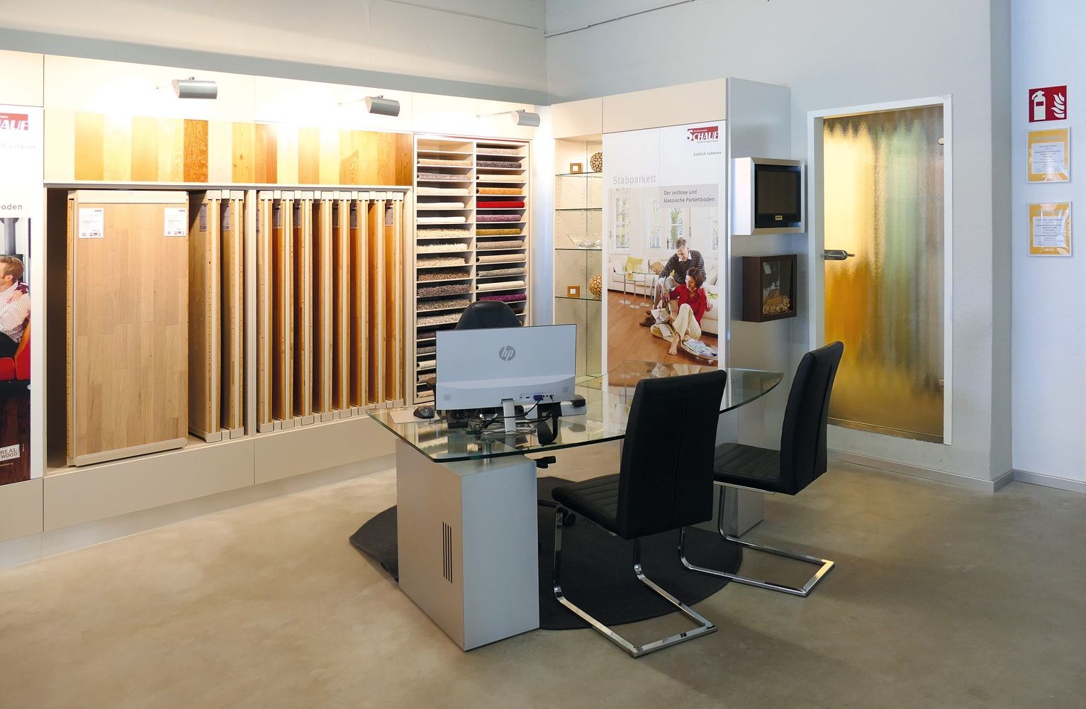 Ausstellungsraum mit Holzfußbodenmustern, einem Glastisch, ergonomischen Stühlen und einer Milchglastür, die für Kundenberatungen gedacht ist.