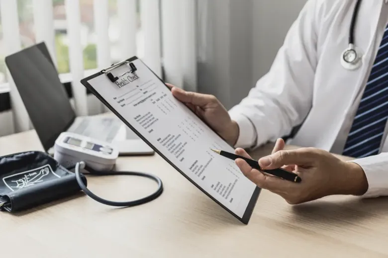Médico sosteniendo un portapapeles, apuntando con un bolígrafo a un formulario médico.