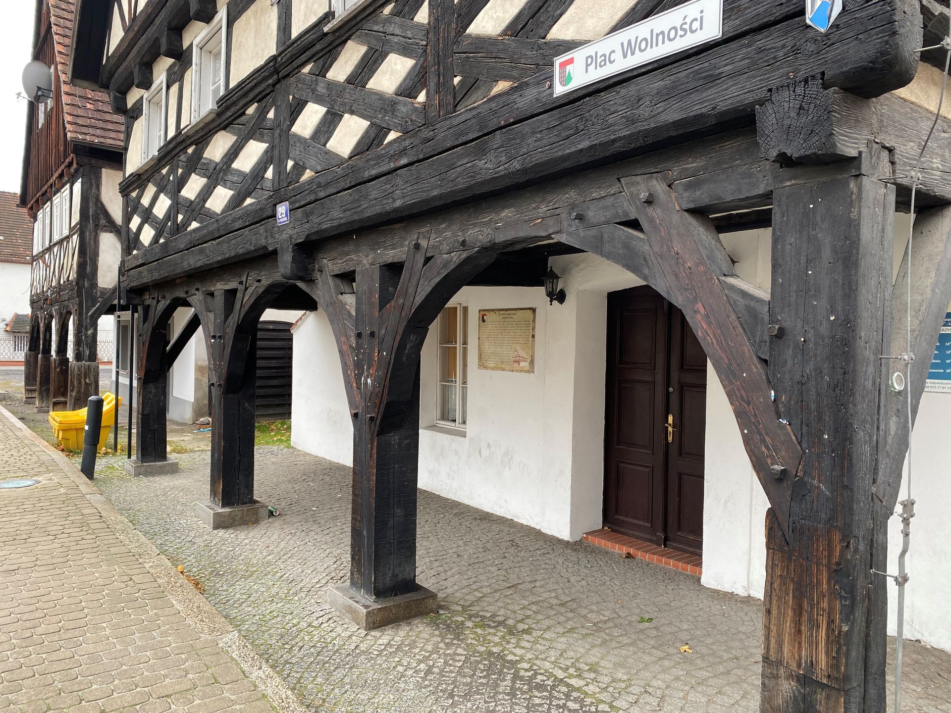 Fachwerkgebäude mit gewölbtem Eingang, dunklem Holzbalken, weißen Wänden und Kopfsteinpflasterweg.