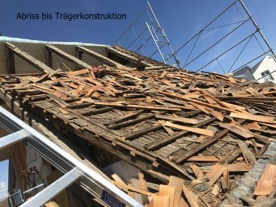Abgerissenes Dach, das Holzbalken und Trümmer unter blauem Himmel freigibt, Gerüst sichtbar.