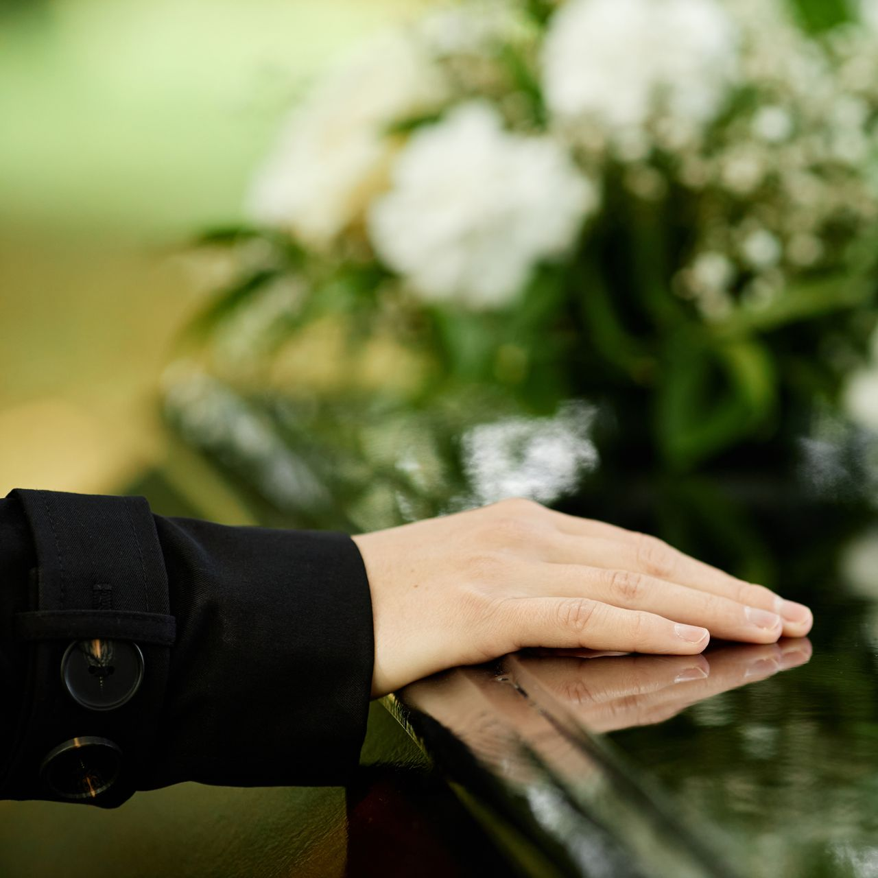Main posée sur une surface sombre près d'un bouquet de fleurs blanches lors d'un service commémoratif.