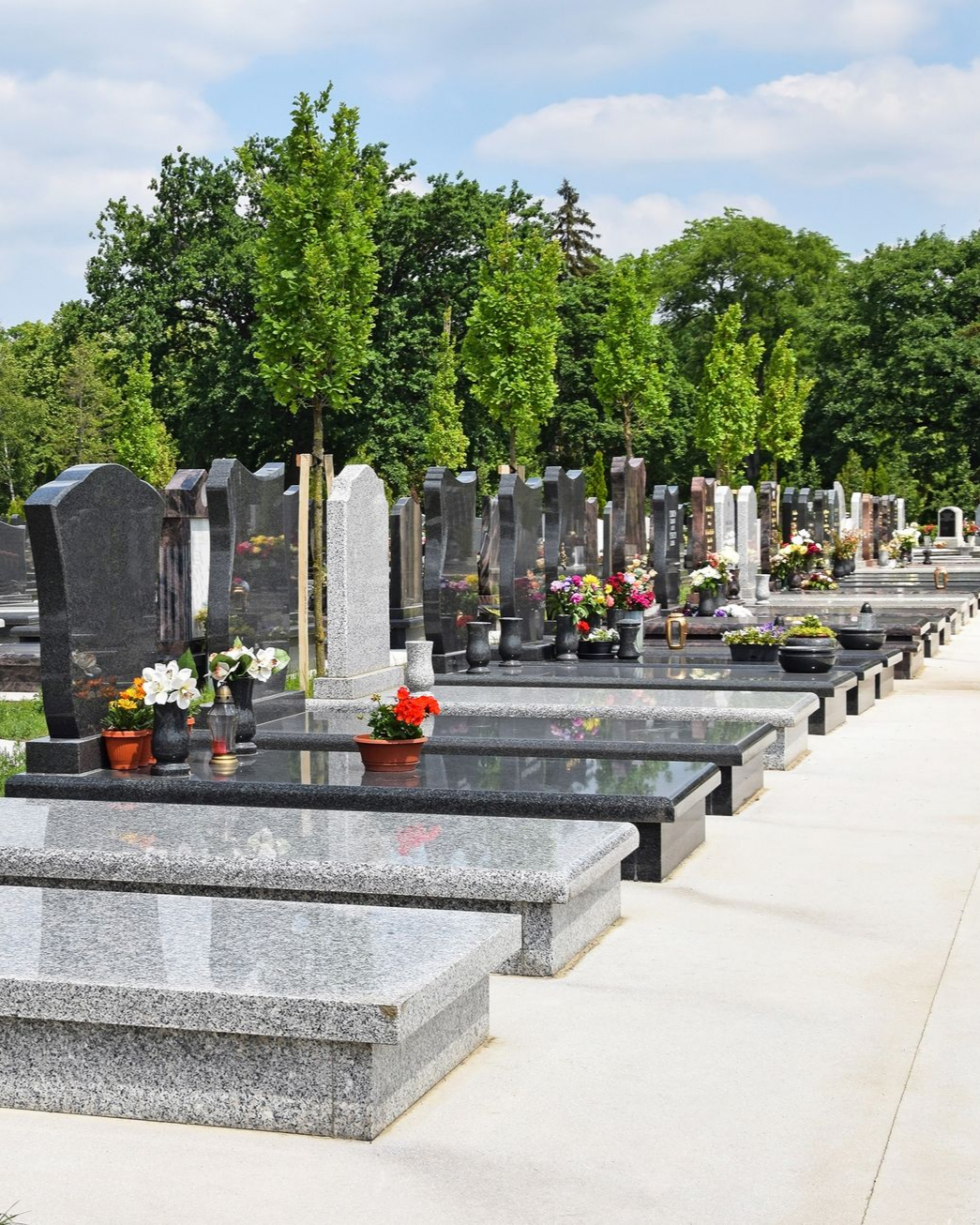 Rangée de pierres tombales blanches dans un atelier ensoleillé, certaines ornées de sculptures et d'inscriptions.