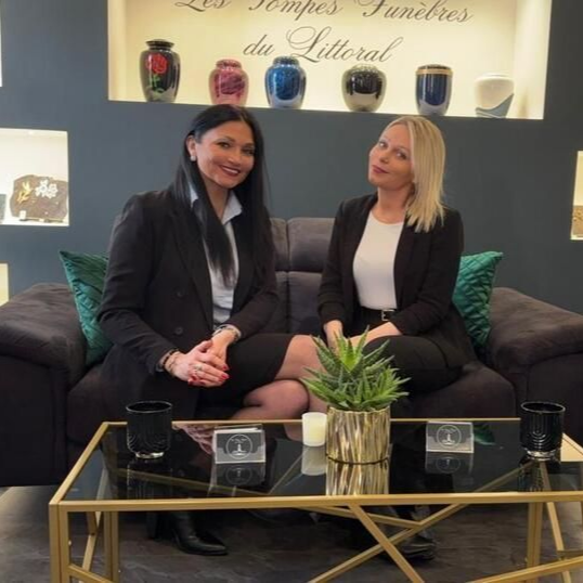 Deux femmes en tenue professionnelle assises sur un canapé dans une maison funéraire.