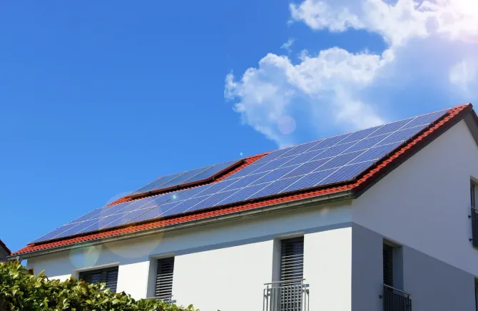 Casa con paneles solares en el techo contra un cielo azul brillante con nubes blancas esponjosas; la luz del sol brilla.
