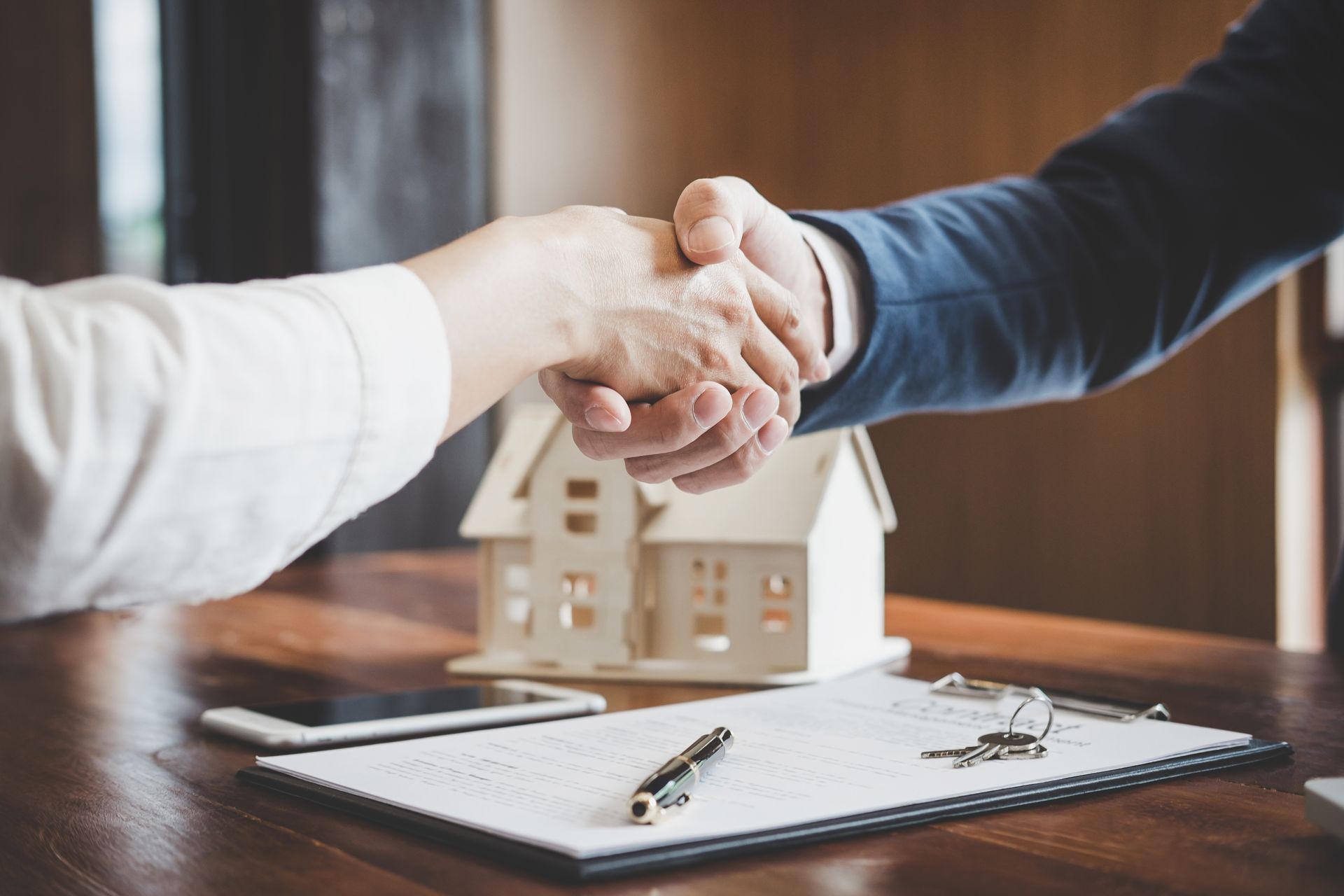 Une poignée de main entre une femme et un avocat avec une maquette de maison posée sur le bureau