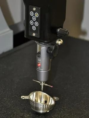 Distributeur alimentaire numérique placé au-dessus d'un bol en métal, déposant une louche d'aliment brun sur un comptoir .