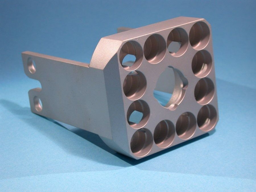 Support métallique usiné avec trous circulaires, présenté sur fond bleu